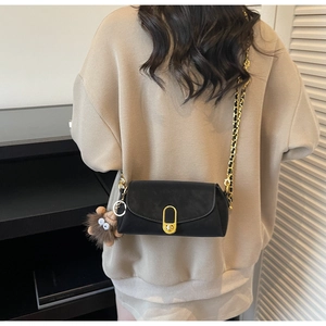Close-up of black crossbody bag with gold buckle, chain strap and plush pendant charm