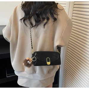 Detail of black crossbody bag with gold chain strap and cute brown plush charm on a model