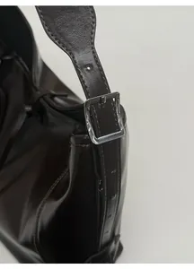 Detail of silver metallic buckle and glossy dark brown leather on the tote bag