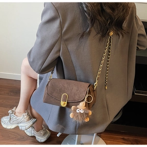 Detail of a brown suede crossbody bag with gold chain strap and playful eye-shaped fur charm