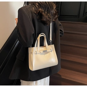 Dettaglio di una borsa tote color crema a tracolla su un blazer nero per un look di classe