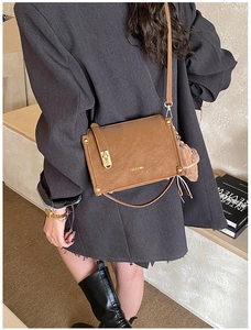 Brown vintage square bag detail with gold clasp, top handle, and plush bear charm