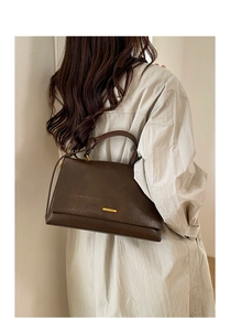 Close-up of dark brown leather handbag featuring gold metal logo and minimalist stitching