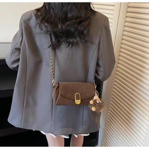 Detail view of a brown leather crossbody bag with gold buckle and plush keychain on a model