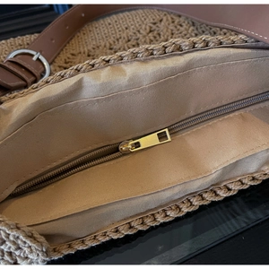 Detail shot of khaki straw tote bag featuring interior lining and secure gold zipper closure