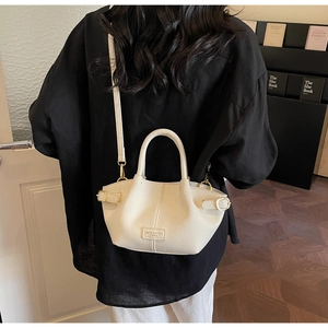 Rear view of a model carrying a beige lychee texture bucket bag with gold hardware