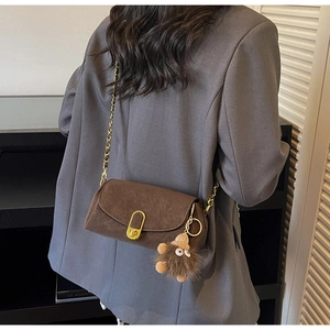 Detailed back view of a dark brown square bag with a plush charm on a model's shoulder