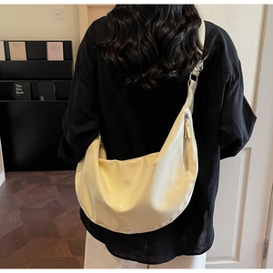 Vue détaillée du grand sac croissant en cuir verni crème porté à l'épaule