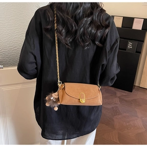 Brown suede shoulder bag with gold hardware and plush charm shown on model's back