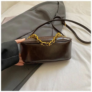 Detail of dark brown vintage crossbody bag with gold chain and glossy leather texture