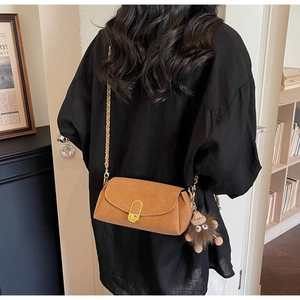 Brown suede crossbody bag with gold U-shaped buckle and plush charm detail on a model
