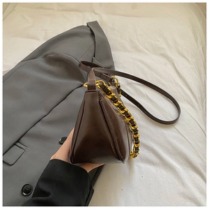 Detail of dark brown glossy leather shoulder bag with decorative thick gold chain strap