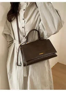 Detail of dark brown leather tote bag with gold metal logo and round top handle
