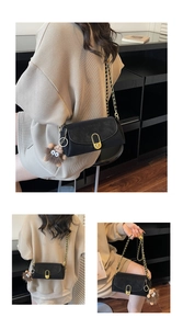 Detail of black leather crossbody bag with gold U-shaped buckle and plush doll charm