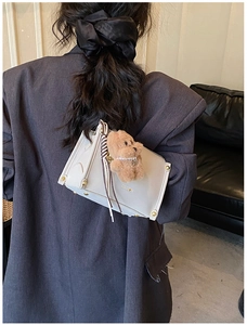 Detail of cream leather square crossbody bag with gold hardware and plush bear charm
