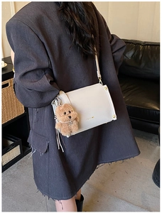 Detail of cream square crossbody bag with gold logo and plush bear charm on a model