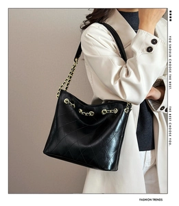 Detail of a large black quilted tote bag with golden chain strap on a model shoulder