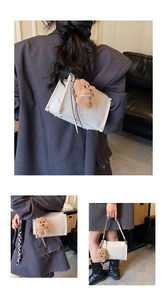 Detail view of cream leather tote with gold logo, teddy bear charm, and striped scarf decor