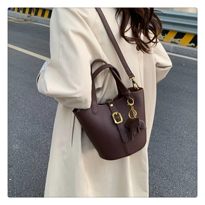 Detail of dark brown lychee grain leather bucket bag with gold buckle and leather charm
