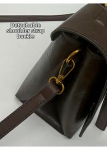 Detail of gold-tone metal buckle and stitching on dark brown faux leather shoulder bag