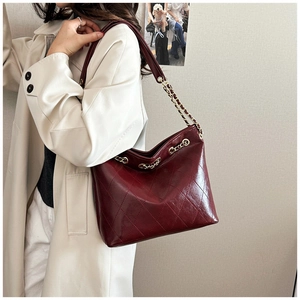 Close-up of quilted burgundy tote bag with gold chain strap on a cream leather coat