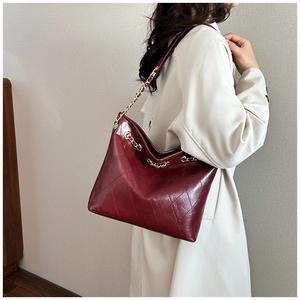 Detail of burgundy quilted tote bag with glossy leather finish and gold chain strap
