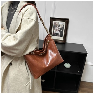Close-up of a large dark brown tote bag featuring classic quilted leather and metal chain straps