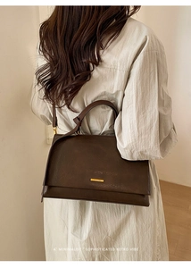 Model wearing dark brown leather shoulder bag with a gold logo and a minimalist retro vibe