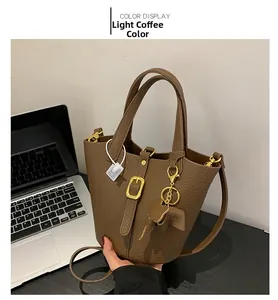 Detail of light coffee bucket bag with lychee texture and elephant charm on desk
