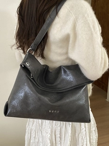 Large dark grey glossy leather tote bag shown on a model for a realistic size reference