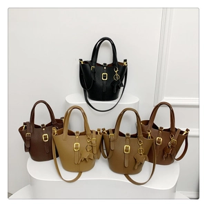 Five assorted colors of leather bucket bags with elephant charms on a white display stand