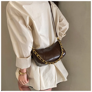 Detail of dark brown glossy leather crescent bag with bold gold chain and strap