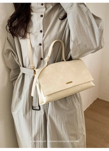 Close-up of a cream minimalist handbag featuring a golden metal nameplate and fine texture