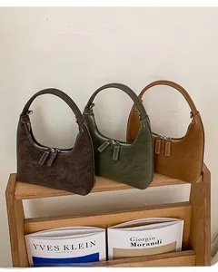 Three half-moon hobo bags in suede leather with dual-zipper closure on a wooden shelf
