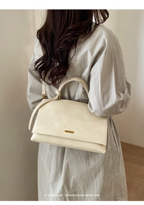 Minimalist off-white leather handbag showing side-view on model with golden metal hardware