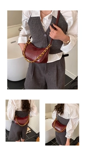 Detail of burgundy crescent bag with thick gold chain strap worn as a shoulder bag