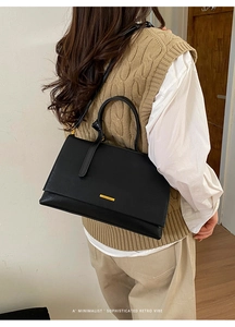 Detailed view of black leather tote bag featuring a gold brand plaque and top handle