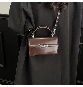 Close-up of brown patent leather handbag with silver twist lock on a black coat