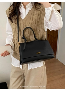 Close-up of minimalist black leather handbag with gold metal bar and top handle