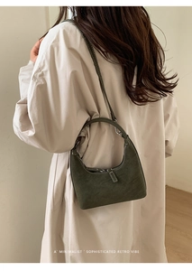 Detail of dark green crescent bag with contrast stitching on a minimalist trench coat