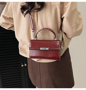 Detail view of burgundy leather handbag with silver lock and detachable strap on model