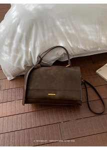 Detail of dark brown leather handbag with gold metal logo and natural wrinkled texture