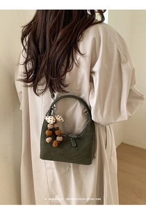 Close-up of dark green matte hobo bag with bow charm and decorative pom poms detail