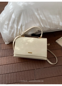 Detail of cream white leather handbag with gold logo plaque on dark wood floor