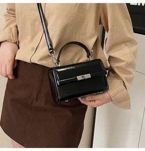 Detailed view of a black patent leather crossbody bag with silver turn-lock and handle