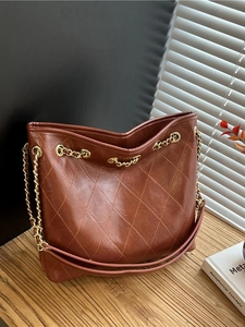 Brown quilted tote bag with golden chain strap and pink handle on a wooden table