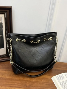 Large black quilted leather tote bag with gold chain strap on a vintage wooden surface