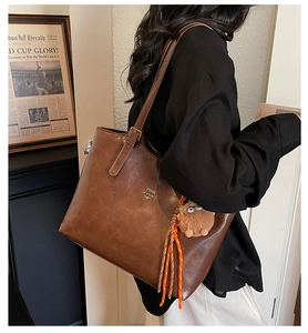 Close-up of brown faux leather tote bag with brand logo and plush monster charm