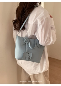 Détail d'un sac seau en cuir bleu clair avec un pendentif d'éléphant de dos sur modèle