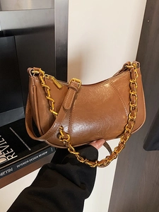 Caramel brown leather underarm bag with gold chain strap on interior design books